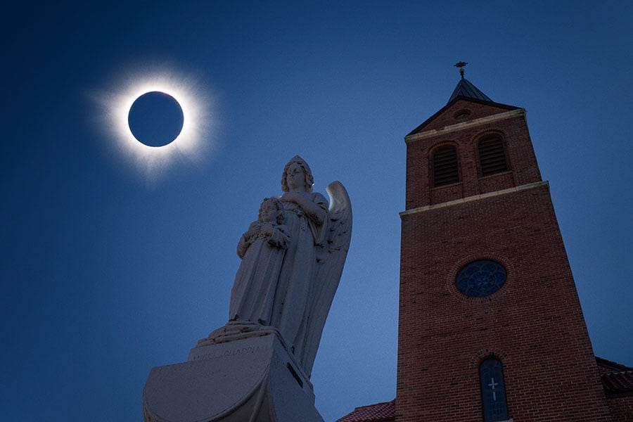 solar eclipse with church spire and statue of angel