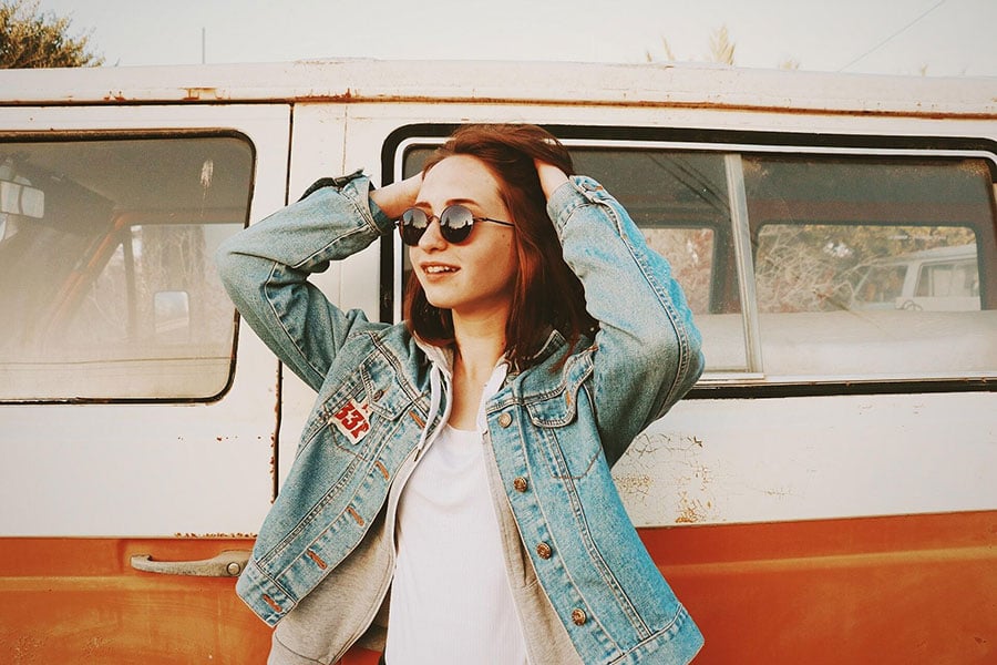 young woman stands in front of old vehicle